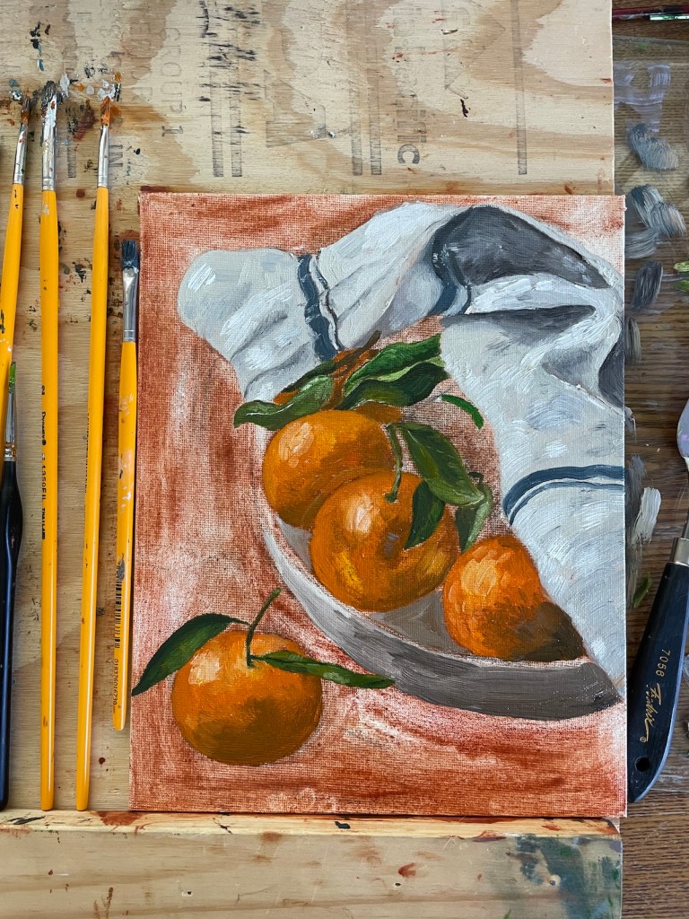Image of an in-progress painting of oranges on a plate next to a towel.